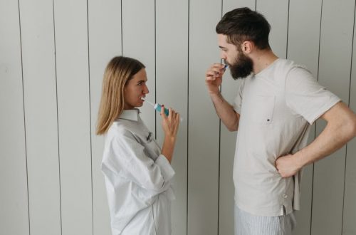 A couple brushing their teeth indoors, sharing a morning routine. Side view highlights interaction.