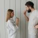 A couple brushing their teeth indoors, sharing a morning routine. Side view highlights interaction.